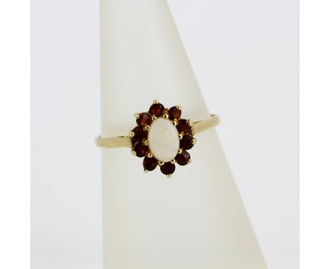 A hallmarked 9ct yellow gold (worn hallmark) cluster ring set with an oval cut opal surrounded by garnets, (M).