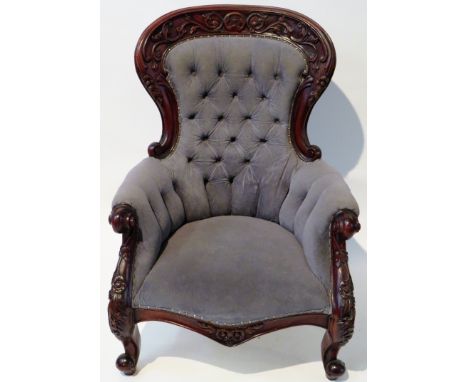 A Victorian armchairWith mahogany show wood, with carved floral detail raised on short scrolled feet, upholstered in grey but