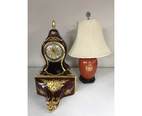 A decorative red and gilt bracket clock with wall bracket together with an Oriental style table lamp with shade