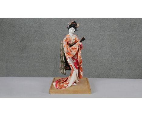 A vintage Japanese geisha girl doll on bamboo base. Dressed in a traditional silk kimono, with paper fan and metal flowers in