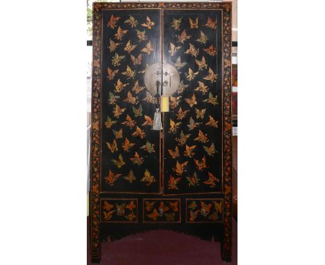 An early 20th century Chinese black and red lacquered wedding cabinet, decorated with butterflies, the two doors enclosing sh