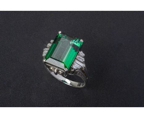 A GREEN TOURMALINE AND DIAMOND RING Set in platinum, the step cut tourmaline flanked by tapered baguette cut diamonds within 