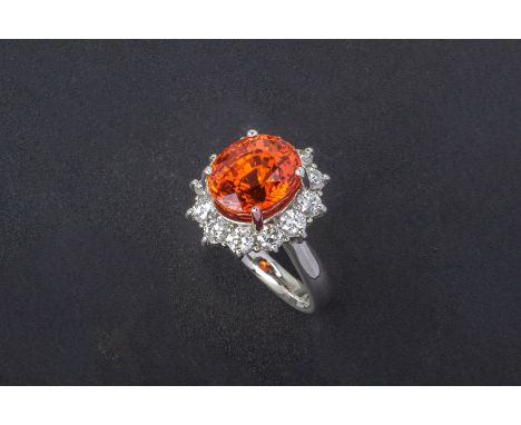 A SPESSARTINE GARNET AND DIAMOND RING Set in platinum, the oval cut garnet within a border of round brilliant cut diamonds  T