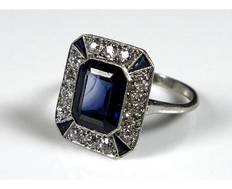 An Art Deco style synthetic sapphire and diamond dress ring, circa 1980, with central emerald cut stone, 9 by 7 by 4.5mm, sur