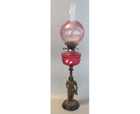 Early 20th century double oil burner lamp, having cranberry globular shade above a cranberry reservoir standing on a metal fi
