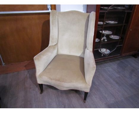An Edwardian wingback fireside armchair on square tapering legs and ceramic castors