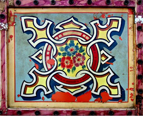 Early vintage painted tin fairground amusement panel with typical floral shield decoration, framed by pine with original hole