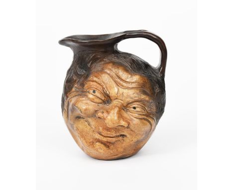 A Martin Brothers stoneware face jug by Robert Wallace Martin, modelled in relief with a smiling face to both sides, glazed b