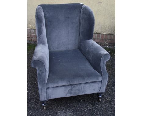 A late Victorian grey/blue plush upholstered country house deep seated wing back fireside chair on ring turned castors
