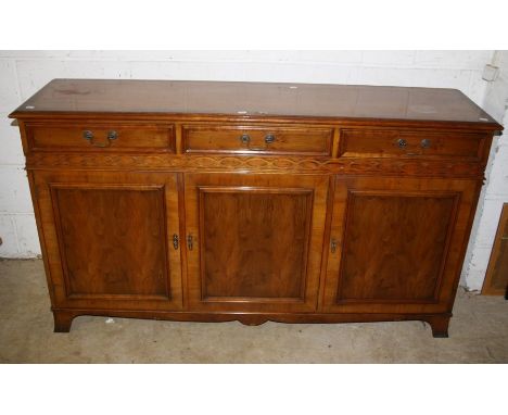 A reproduction Yew veneered and crossbanded low dresser fitted three drawers over ribbon frieze and cupboard doors on bracket