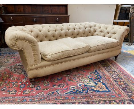 A late Victorian Howard style button back upholstered chesterfield sofa raised upon turned front supports to castors, rear le