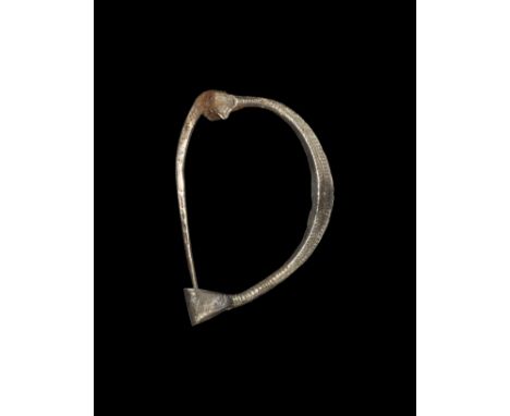 5th-1st century BC. A lozenge-section silver bow with trapezoidal catchplate, flared terminal with hinged square-section pin;