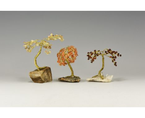 A group of three small gem trees with brass wire trunks and branches, the branches tipped with tumblestones, one of garnet wi