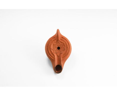 An undated archaistic hollow-formed ceramic oil lamp with broad nozzle, fin handle, discus with wreath to the shoulder, raise
