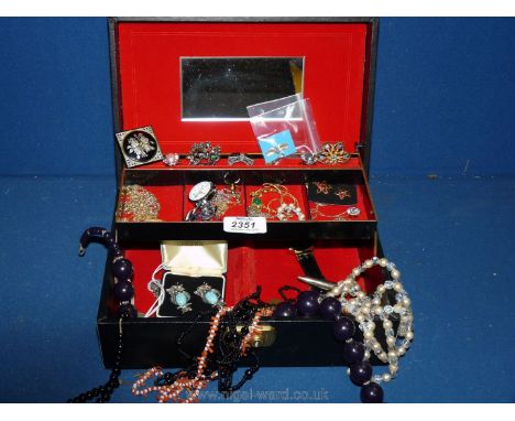 A large black jewellery box with key, containing a mixed variety of necklaces, earrings, brooches, costume rings, tie pins an