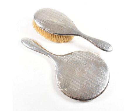 A 1920's hallmarked silver mounted vanity mirror and hairbrush. Each having an engine turned repeated stripe pattern with cen