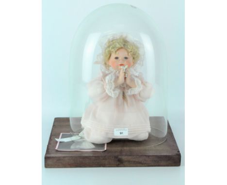 A 20th century glass dome mounted on a wooden base, height 40cm, containing a ceramic doll positioned on her knees is a prayi