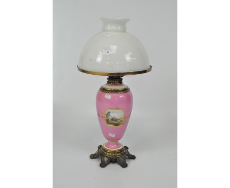 A pink porcelain vase form lamp decorated with landscape vignettes and gilt details, on a metal foot, with white glass shade,