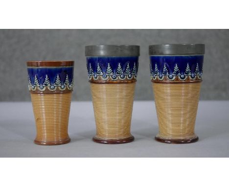 Three Doulton Lambeth glazed ceramic foliate design beakers. Two the same size with pewter rims and one smaller. Impressed ma