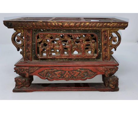 A Chinese wooden tea pot stand in red and gilt with carved and pierced decoration of figures and resting on dragons heads, ht