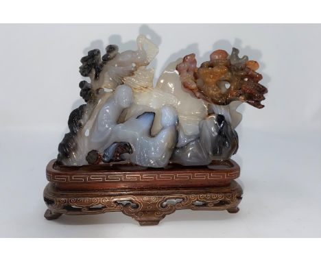 A Chinese agate coloured stone carving of 2 people playing a board game, on base (not matching)(some restoration) length 14.5