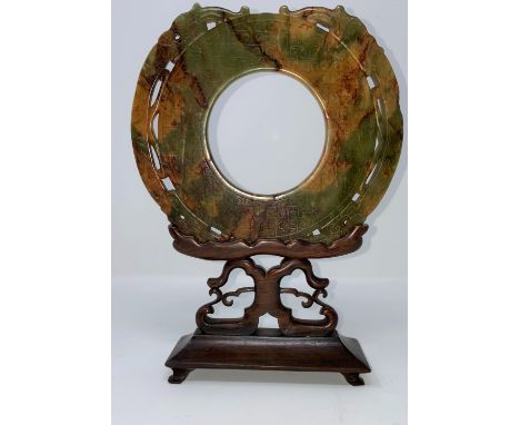 A Chinese carved jade colour stylized circular stone with incised decoration, on hardwood stand (restored) overall height 26c