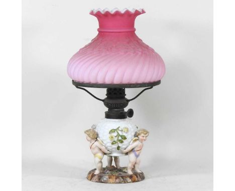 An early 20th century Dresden porcelain oil lamp, having a basketweave font, encrusted with flowers, on three cherub supports