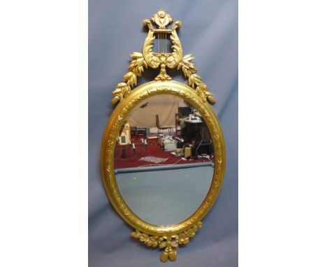 A Regency style giltwood oval mirror with carved harp and floral crest, having bevelled glass plate, 135cm x 67cm