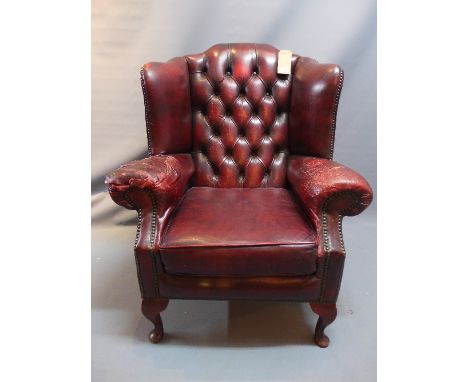 A 20th Century red leather wing back armchair with button back upholstery raised on cabriole legs (a/f), 