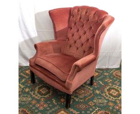 An upholstered button backed winged armchair