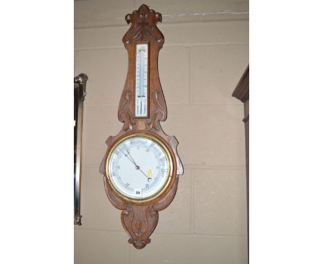 An aneroid barometer and thermometer mounted in a carved and stained oak banjo pattern mount (slightly incomplete).