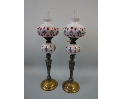 A PAIR OF BOHEMIAN OVERLAID OPAQUE GLASS OIL LAMPS, the matching ruby overlaid glass with opaque floral painted reservoir and
