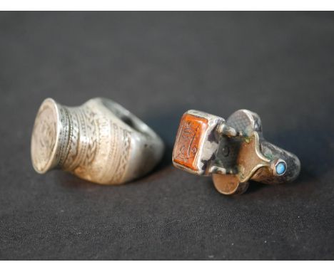 Two Islamic white metal seal rings, one with an orange moulded glass panel with calligraphic design and engraved detailing to
