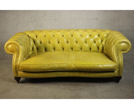A yellow leather Chesterfield two seater sofa by Baxter - Italy, with a buttoned back and scrolling arms, on turned supports.