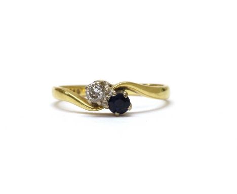 An 18ct gold two stone diamond and sapphire crossover ring, with a brilliant cut diamond and a circular mixed cut sapphire, c