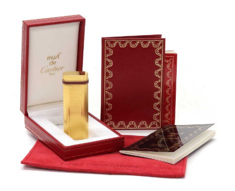 A cased Must de Cartier gold plated gas lighter, c.1990, of oval rectangular form with engine turned decoration and a red lac