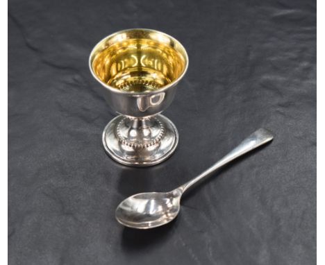 An Elizabeth II cased silver egg cup and spoon set, having a slightly flared rim and beaded decoration on a circular step mou