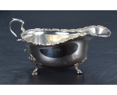 A George V silver sauce or gravy boat of traditional design, with Chippendale style rim, generous spout opposed by a scrollin