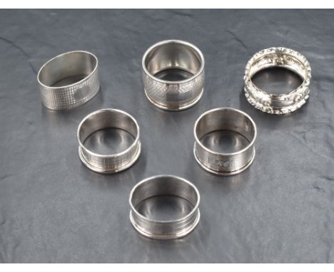 A group of six silver napkin rings, five having engine turned decoration and cartouches, the other having lobed rims and embo