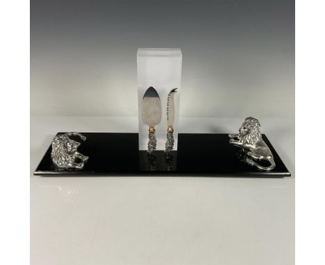 A black marble cutting board featuring two resting lions at one end, accompanied by a pair of stainless-steel cheese knives, 