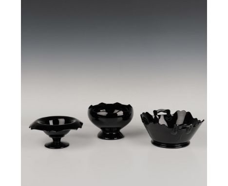 A set of three black glass bowls, one with a wavy rim and ridged base, another with a flower-like rim and flat base, and a th