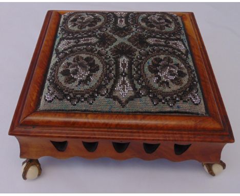 A Victorian square mahogany footstool with beaded tapestry upholstery and original gilt claw feet with ceramic castors, 16 x 