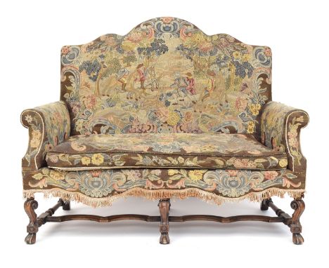 A Queen Anne style two seater sofa, needlework upholstery, the shaped back over outscrolled arms, on carved legs and braganza