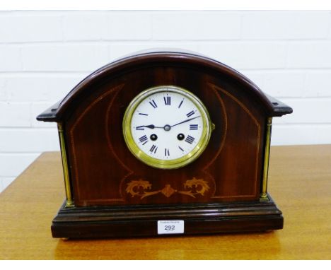 A mahogany and inlaid mantle clock, the domed top over a white enamelled dial with Roman numerals flanked by brass pilasters 