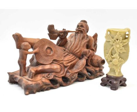 An early 20th century carved wooden figure of a resting fisherman smoking a pipe, the fish in his hand with porcelain eyes, w