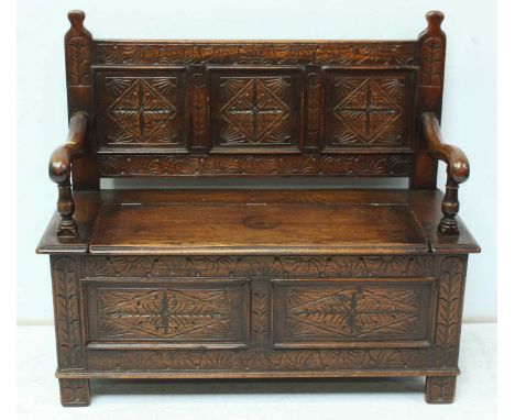 A 1930s oak two seater settee, in the 18th century style, with carved panel back, shaped open arms, lift up seat and panelled