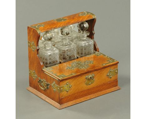 A late Victorian oak brass bound tantalus, fitted with three decanters and two compartments, one housing glasses, and with fu