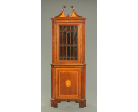 An Edwardian inlaid mahogany standing corner cupboard, with swans neck pediment above a glazed door with wooden astragals, th