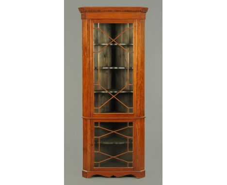 An Edwardian inlaid mahogany standing corner cupboard, with moulded dentil cornice above a glazed upper door enclosing shaped