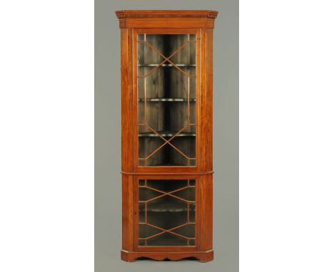 An Edwardian inlaid mahogany standing corner cupboard, with moulded dentil cornice above a glazed upper door enclosing shaped